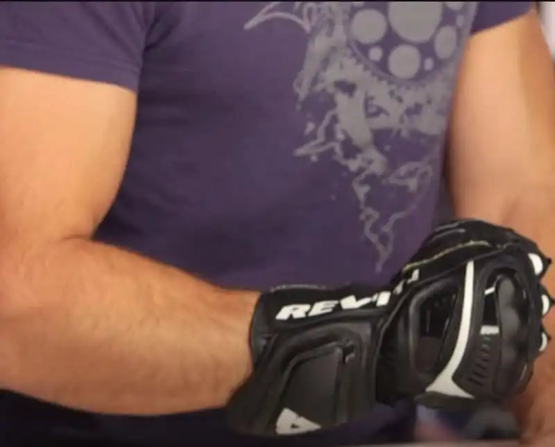The image shows a man wearing REV’IT! Jerez 3 motorcycle gloves. The gloves are black with white accents and have "Rev'it" branding on them, indicating they are made by the Rev'it motorcycle gear company.